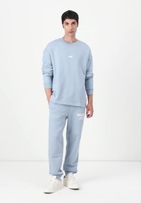 Lichtblauwe katoenen sweatshirt met ronde halslijn en logo, gecombineerd met bijpassende lichtblauwe joggingsbroek met een gedrukt accent. Witte sneakers.