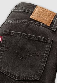 Donkergrijze spijkerbroek van denim met een tan leren patch met reliëflogo, een achterzak met contrasterende stiksels en een rode label aan de zijkant.