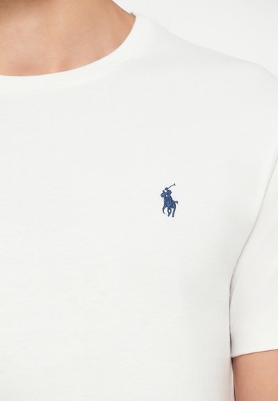 T-shirt branca de algodão com decote redondo e mangas curtas. Apresenta um logótipo de jogador de polo bordado em azul marinho no peito.