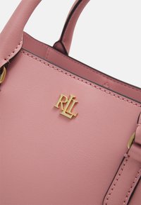 Rosa läderhandväska med ett guldhardware-logotyp (RL) och kontrasterande sömmar. Kompakt design med korta handtag och mjuk textur.