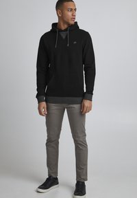 Felpa nera con cappuccio e tasca a marsupio, dettagli grigi e lacci. Abbinata a pantaloni grigi chiari e sneakers nere. Look semplice e informale.