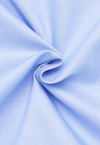 Tessuto di un blu chiaro con una texture che presenta un aspetto liscio e intrecciato, caratterizzato da un motivo sottile. Il materiale è morbido e flessibile, adatto a vari utilizzi.