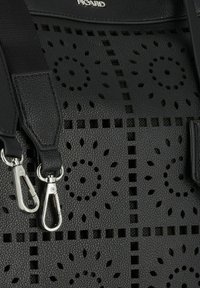 Borsa in pelle nera perforata con ritagli geometrici, hardware in argento e spallacci regolabili con ganci girevoli. La superficie testurizzata aggiunge dettagli.