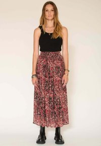 Un débardeur noir à côtes associé à une longue jupe maxi fluide avec un motif floral abstrait en rose, rouge et noir. Bottes noires chevilles.