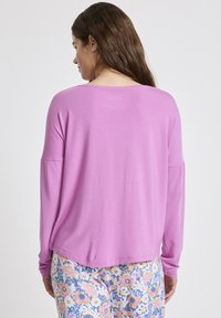 Helles rosa Langarmoberteil mit lässiger Passform, rundem Halsausschnitt und weichem Material. Kombiniert mit Blumenmusterhosen.