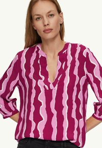 Fuchsia shirt met een V-hals en lange mouwen, voorzien van een golvend roze en witte patroon. Gemaakt van lichtgewicht stof.