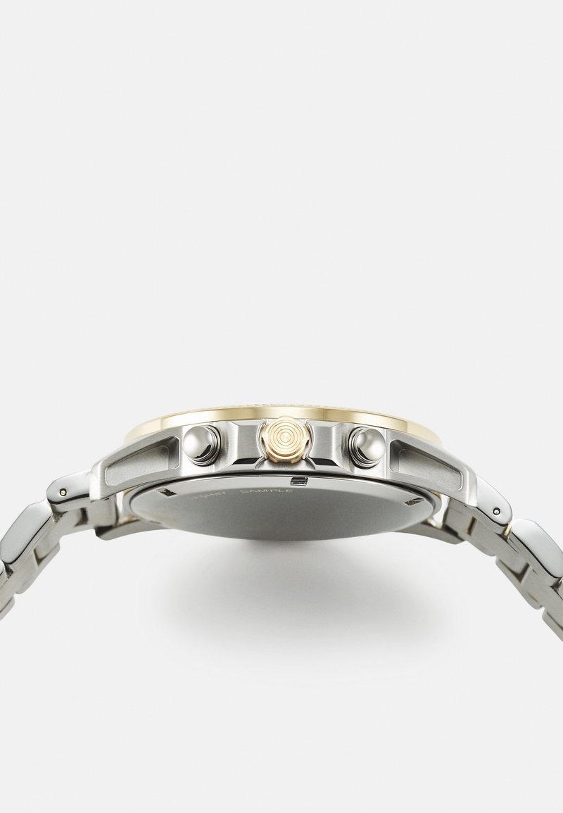 Montre pour homme avec un boîtier en acier inoxydable rond, des accents dorés et un bracelet en argent. Comprend deux poussoirs et une couronne texturée.