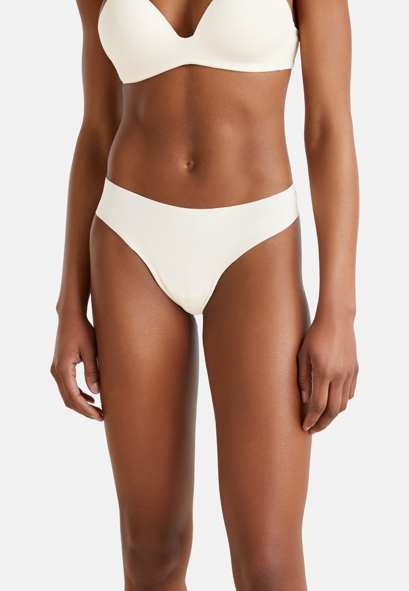 Crème-kleurige bikinionderbroek met een gladde, matte textuur, een low-rise ontwerp en brede zijkanten, die een minimalistische stijl benadrukt.