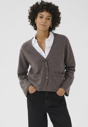 Brauner Strickcardigan mit V-Ausschnitt, drei Knöpfen, zwei Fronttaschen und gerippten Bündchen. Trägt man über einem weißen Hemd mit Kragen, im cropped Fit.