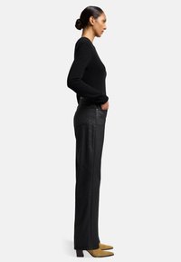 Maglione nero a maniche lunghe abbinato a pantaloni neri a vita alta e gamba dritta. Le scarpe sono beige con punta affusolata e tacco chunky.