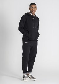 Svart hoodie med rutigt foder, dragsko för stängning och logotypdetalj. Matchas med svarta joggers och mönstrade sneakers.