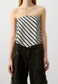 Haut sans bretelles en satin blanc avec des rayures diagonales noires ; design lâche et court ; associé à un pantalon ample vert olive avec des détails en métal.