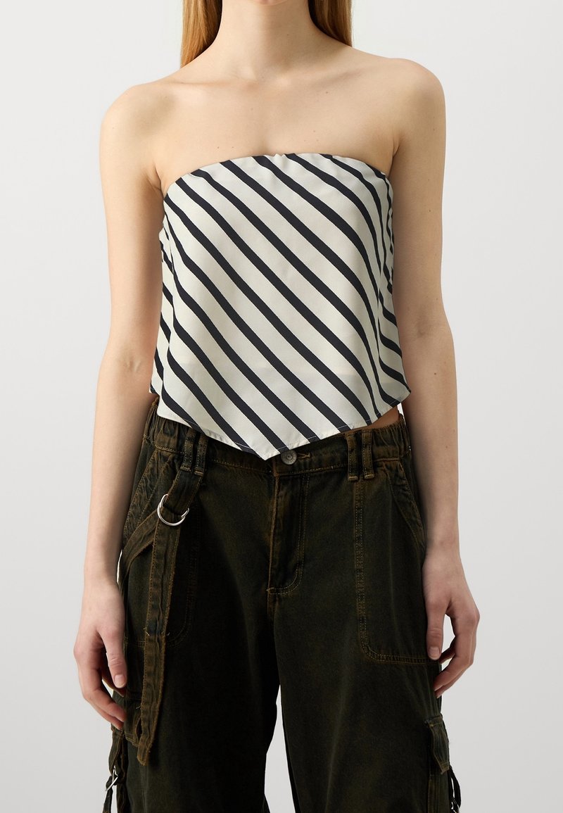 Haut sans bretelles en satin blanc avec des rayures diagonales noires ; design lâche et court ; associé à un pantalon ample vert olive avec des détails en métal.