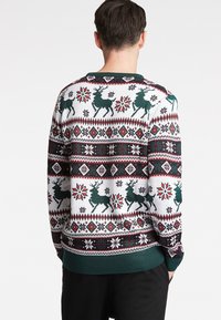 Sweater branco tricotado com um padrão festivo que apresenta renas verdes, formas geométricas em vermelho e preto, e barras e punhos em verde escuro.