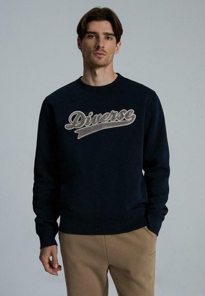 Granatowy sweatshirt wykonany z miękkiego materiału, z haftowanym logiem "Diverse" w kolorze srebrnym. Klasyczny okrągły dekolt i ściągacze.