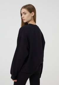Felpa nera oversize, collo a giro, spalle scese, polsini e orlo a costine, tessuto morbido, vestibilità rilassata, design semplice senza loghi.