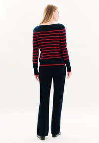 Navy- und rot gestreifter Pullover mit weitem Ausschnitt, kombiniert mit weit ausgestellten schwarzen Hosen. Weiche Textur, lässiges Design und nahtlose Verarbeitung.