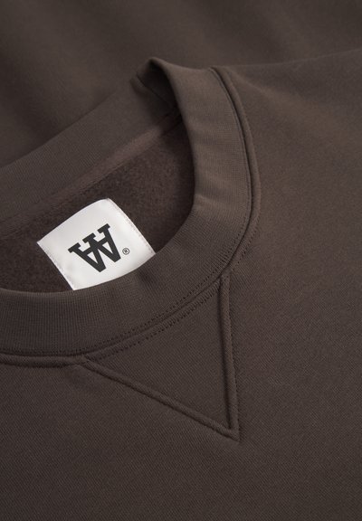 Sweatshirt marron foncé avec un col côtelé, des coutures flatteuses et une étiquette blanche avec un logo noir. Texture douce et design décontracté.