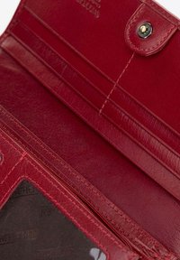L'interno del portafoglio in pelle rossa presenta scomparti per carte, una tasca con zip e una finestra trasparente per l'ID. Texture liscia con cuciture dettagliate.