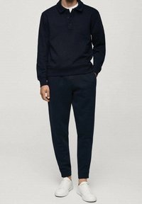 Námořnická modrá mikina s límečkem a třemi knoflíky, doplněná o odpovídající zúžené tepláky a bílé tenisky. Měkká textilní struktura.