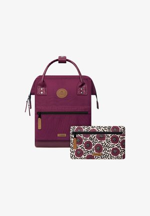 Sac à dos en tissu violet profond avec des accents en cuir, comportant un logo rond et une poche zippée à l'avant. Accompagné d'une pochette à motifs.