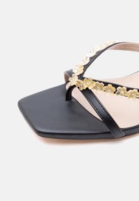 Μαύρο σανδάλι με τετραγωνισμένη μύτη και δύο λεπτές λουρίδες διακοσμημένες με μικρά χρυσά λουλούδια και διαυγή κρύσταλλα.