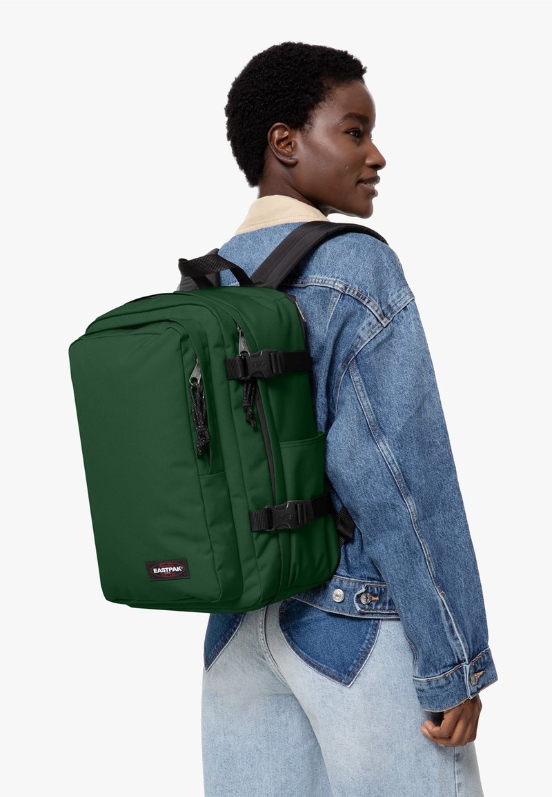 Grön ryggsäck med två framfickor, justerbara remmar och spänne-lås. Tillverkad av hållbart material med en slät matt yta.