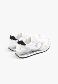 Zapatillas blancas con detalles de ante gris, que cuentan con un talón negro y un logo de calavera. Diseño con cordones, con una parte superior texturizada y suela de goma negra.