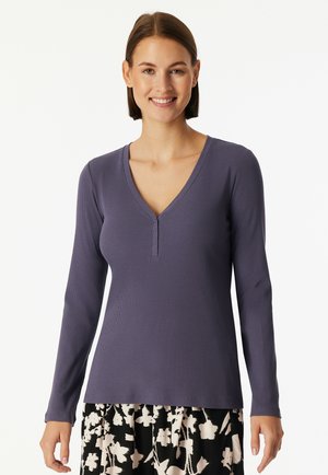Long-sleeve, V-neck top in dark purple ribbed fabric with a three-button placket. Paired with a floral patterned black and white skirt.