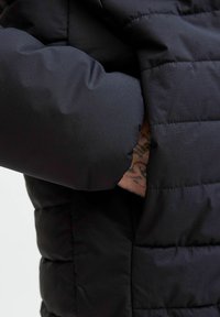 Czarna kurtka puchowa z teksturowanym, pikowanym wzorem; posiada dopasowany mankiet i boczną kieszeń. Materiał wydaje się gładki i trwały.
