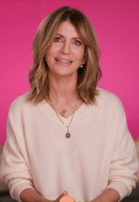 Cream-colored, oversized sweater with V-neck; layered chains featuring a heart-shaped pendant and a teardrop charm; soft texture.