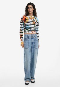 Langärmliges Oberteil mit floralem und gestreiftem Design in lebhaften Farben, kombiniert mit locker sitzenden hellblauen Jeans aus Denim mit großen Taschen.