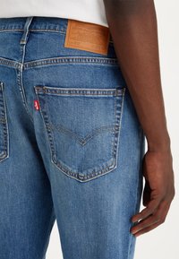 Blå denimjeans med rak passform. Märkbar läderpatch på baksidan av midjan. Har en klassisk femfickdesign och synlig sömnad.