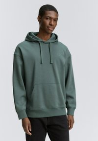 Sudadera verde con capucha, bolsillo tipo canguro y cordones. Fabricada con una suave tela texturizada, presenta un logo sutil en el pecho.