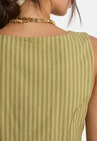 Πράσινο ριγέ αμάνικο τοπ από υφασμάτινη υφή, με τετράγωνο ντεκολτέ και μικρό χρυσό ταμπελάκι στο πίσω μέρος του λαιμού.