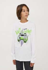 T-shirt bianco a maniche lunghe con un grafico di un controller di gioco verde e nero, accompagnato dal testo "Re del Gioco", "Gioca" e "Nuovo Livello".
