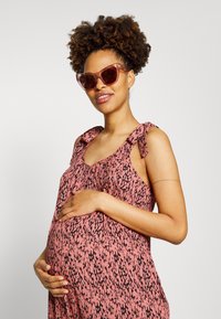 Vestido rosa com padrão, com alças de laço e um ajuste solto. Acompanhado de óculos de sol transparentes, apresentando uma textura suave e um tecido macio.