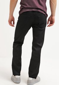 Vaqueros de mezclilla negra con un corte ajustado, cinco bolsillos y una textura suave. Combinados con zapatillas deportivas de color gris claro, mostrando un estilo casual.