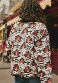 Mønstret jakke med en beige bund, sorte tigerstriber og kraftige orange og pink blomsterprint, med en rund halsudskæring og lange ærmer.