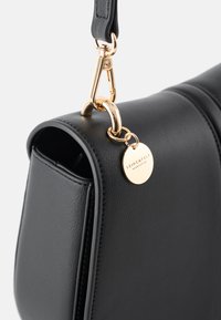 Black leather handbag with a curved shape, gold hardware, and a round metal tag engraved with "SEIDENFELT." Smooth texture and clean lines.