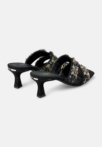 Le mule nere con tacco alto presentano un morbido materiale in suede, cinghie incrociate decorate con embellishments metallici e gemme, e un design del tacco scolpito.