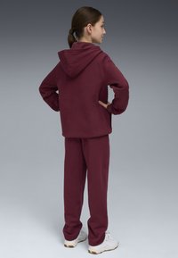 Felpa con cappuccio color marrone e pantaloni abbinati. Tessuto morbido, vestibilità ampia e tasca a marsupio. Scarpe da ginnastica bianche completano l'outfit.