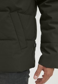 Dunkelgrüne Daunenjacke mit Seitentasche und strukturiertem Stoff. Verfügt über ein sichtbares Logoetikett an der linken Naht, weiches und isoliertes Design.