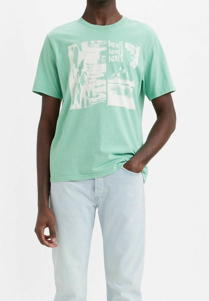 T-shirt en coton vert menthe avec des motifs graphiques abstraits blancs. Manches courtes, col rond, coupe décontractée, porté avec un jean bleu clair.
