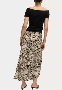 Schwarzes Off-Shoulder-Oberteil kombiniert mit einem beigen und schwarzen Tiermuster-Maxikleid, das ein lockeres Design und einen weichen Stoff aufweist.