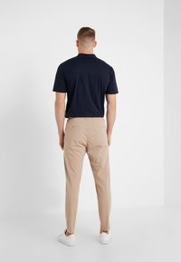 Granatowa koszulka polo w parze z jasnobeżowymi, zwężanymi chinosami. Oba elementy mają minimalistyczny design; model stoi w białych trampkach.