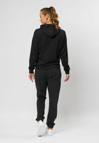 Zwarte hoodie en bijpassende joggers, gemaakt van een katoenmix, met aansluitende boorden en tailleband, voorzien van een capuchon, gecombineerd met witte sneakers.