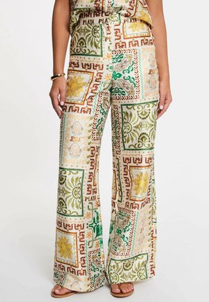 Pantaloni a gamba larga con motivi multicolori di sole, conchiglie e fiori in tonalità di verde, giallo e marrone, indossati con sandali e top coordinato.