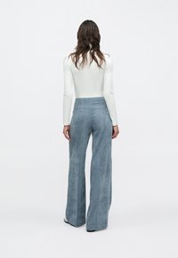 Lyseblå bredbenede bukser i fløjl med højtaljet snit, prydet med lodrette riller og en glat tekstur, set bagfra.