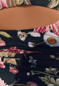 Blommönstrad tyg med svart bakgrund, prydd med rosa, vita och gröna blommor; inkluderar detalj med metallspänne och rynkad design.